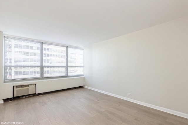 spare room with light wood-type flooring, baseboards, and an AC wall unit