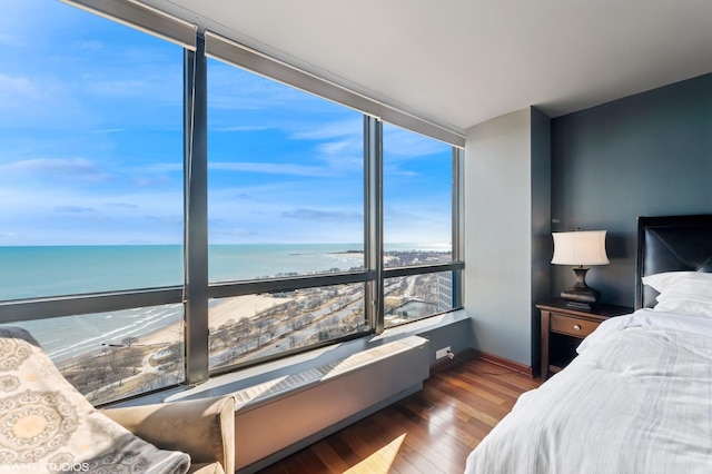 bedroom featuring a wall of windows, a water view, and wood finished floors