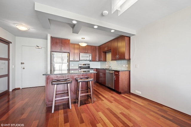 kitchen with a sink, tasteful backsplash, appliances with stainless steel finishes, a breakfast bar area, and light wood finished floors