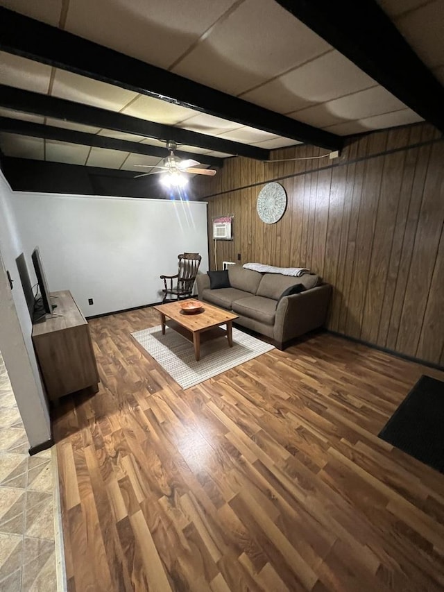 unfurnished living room with wood walls, wood finished floors, beam ceiling, and a ceiling fan