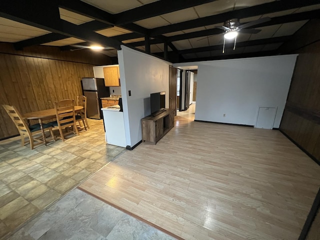 interior space with beamed ceiling, light wood finished floors, wood walls, and a ceiling fan