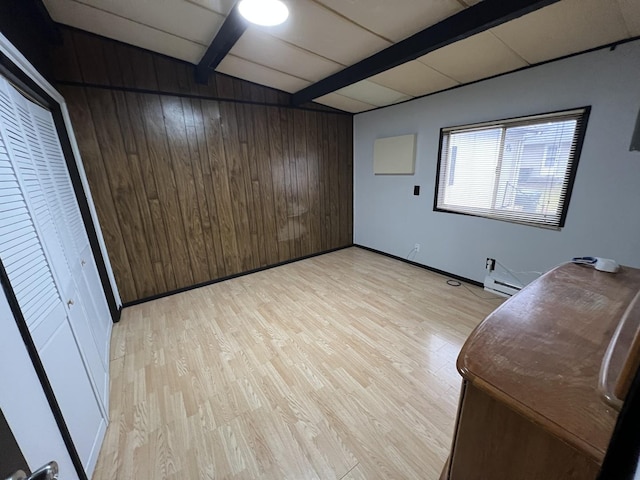 unfurnished room with light wood finished floors, wood walls, beam ceiling, and baseboards