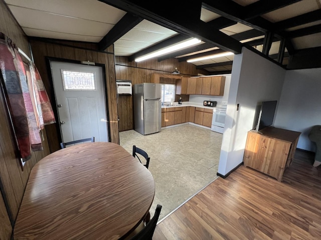 kitchen with electric range, beamed ceiling, freestanding refrigerator, light countertops, and wood walls