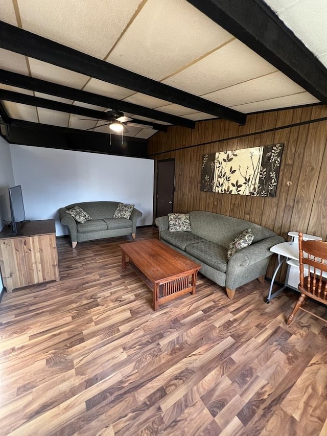 living area with ceiling fan, wood finished floors, beam ceiling, and wooden walls