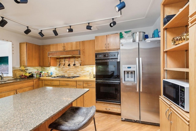 kitchen featuring light wood-style floors, a sink, stainless steel appliances, under cabinet range hood, and backsplash