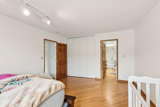 bedroom with a closet, baseboards, ensuite bath, light wood-style floors, and track lighting