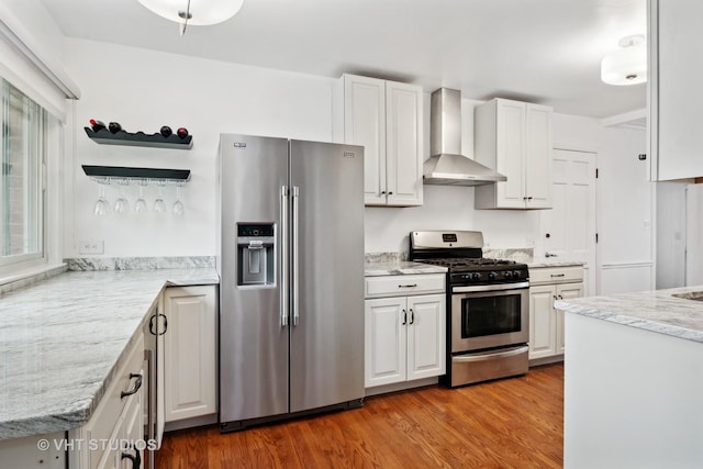 kitchen featuring stainless steel appliances, wall chimney exhaust hood, white cabinetry, and light stone countertops