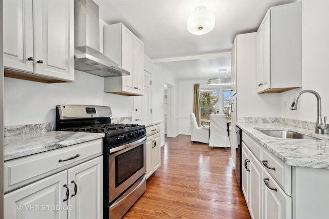 kitchen with stainless steel gas stove, light wood-style flooring, wall chimney range hood, white cabinetry, and a sink