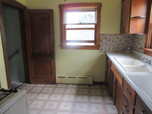 kitchen with a sink, baseboard heating, light countertops, light floors, and backsplash