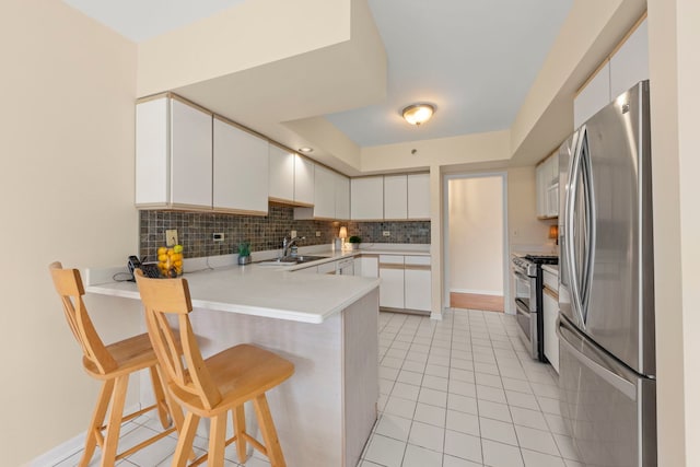 kitchen featuring appliances with stainless steel finishes, a peninsula, a sink, decorative backsplash, and light tile patterned floors