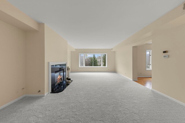 unfurnished living room with carpet floors, baseboards, and a glass covered fireplace