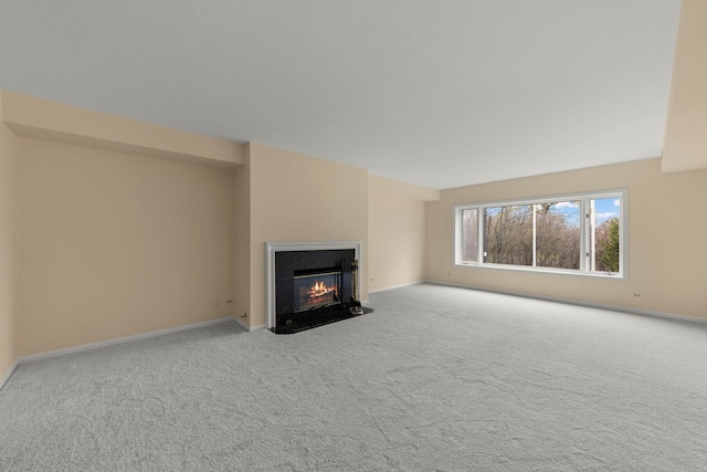 unfurnished living room featuring carpet, a fireplace with flush hearth, and baseboards