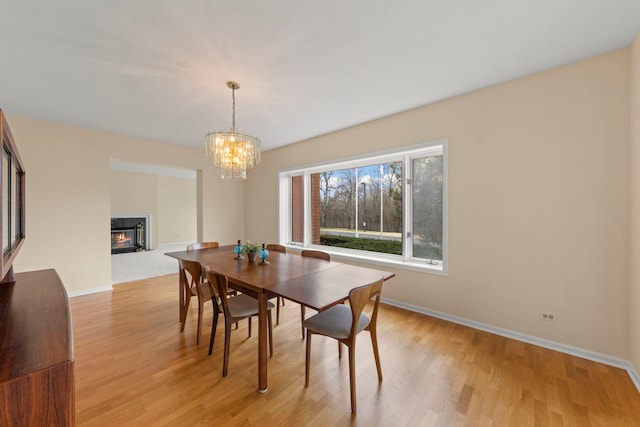 dining space with light wood-style floors, a chandelier, baseboards, and a glass covered fireplace