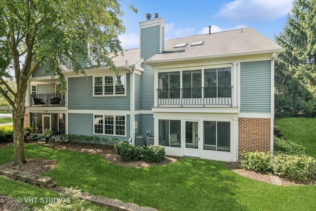 back of property featuring a shingled roof, a balcony, a chimney, a yard, and brick siding