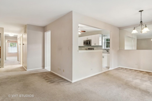 kitchen with light carpet, white cabinetry, light countertops, stainless steel microwave, and pendant lighting