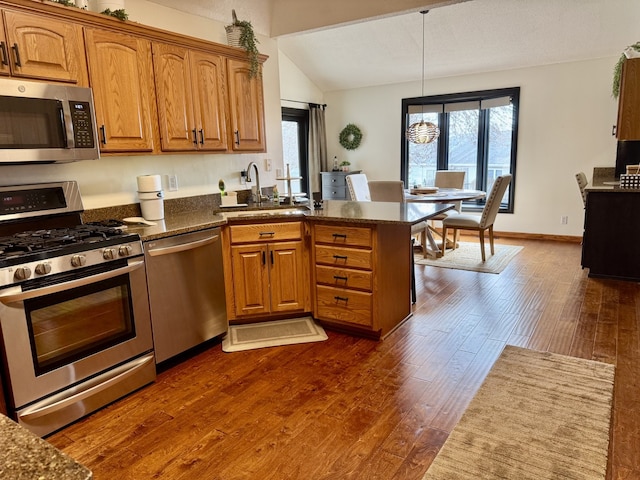 kitchen with appliances with stainless steel finishes, dark wood-style flooring, brown cabinetry, and a sink