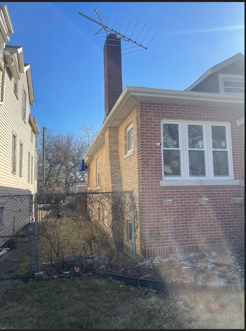 view of side of home featuring brick siding, fence, and a chimney