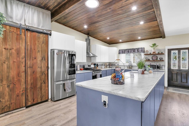 kitchen with light wood finished floors, a center island, wall chimney range hood, appliances with stainless steel finishes, and open shelves