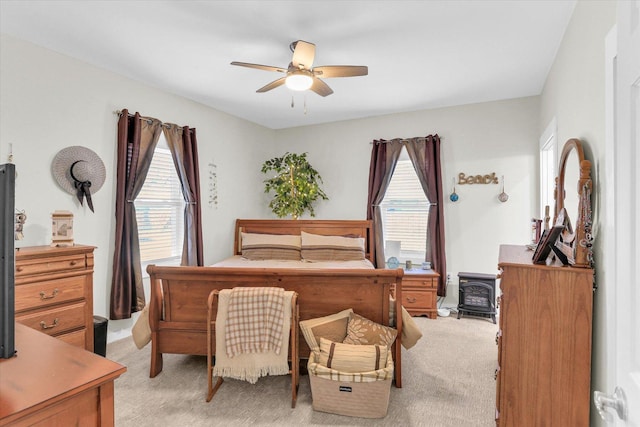bedroom with a ceiling fan, light colored carpet, and a wood stove