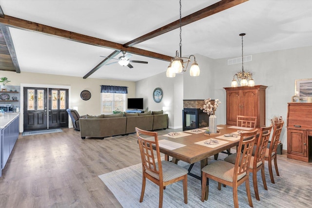 dining room featuring visible vents, a multi sided fireplace, beam ceiling, light wood-style flooring, and ceiling fan with notable chandelier