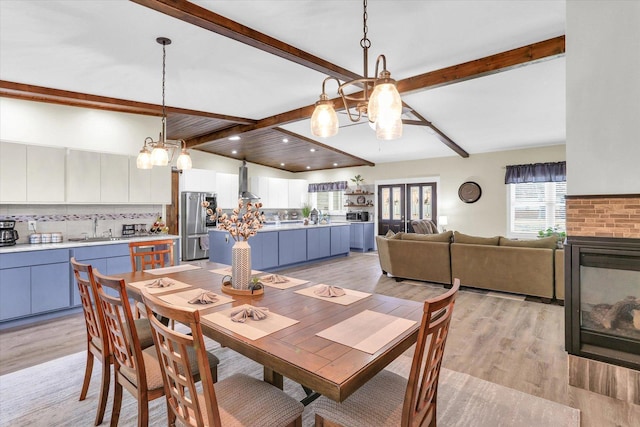 dining room featuring vaulted ceiling with beams, recessed lighting, a multi sided fireplace, light wood-type flooring, and a chandelier
