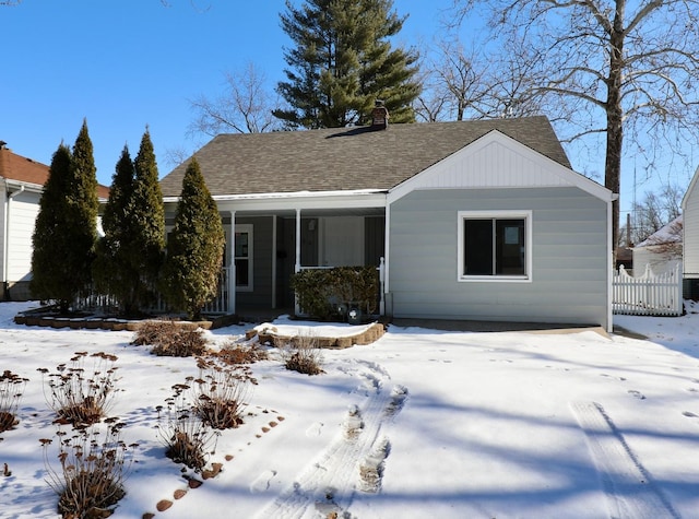 view of front facade featuring a shingled roof, fence, and a chimney