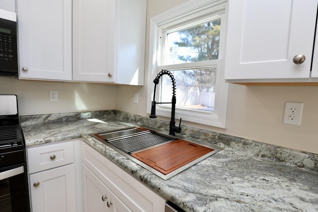 kitchen with white cabinetry, light stone counters, a sink, and oven