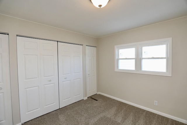 unfurnished bedroom featuring carpet floors, baseboards, and two closets