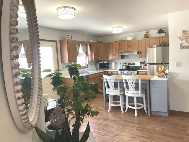 kitchen featuring brown cabinetry, appliances with stainless steel finishes, light countertops, a kitchen bar, and a sink