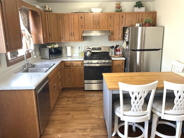 kitchen with brown cabinets, light countertops, appliances with stainless steel finishes, a sink, and under cabinet range hood