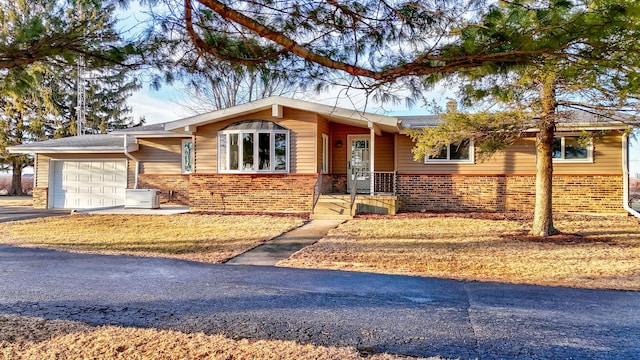 view of front facade with a garage, driveway, brick siding, and central AC unit