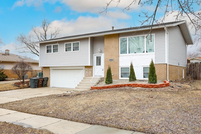 bi-level home featuring an attached garage, fence, concrete driveway, and brick siding