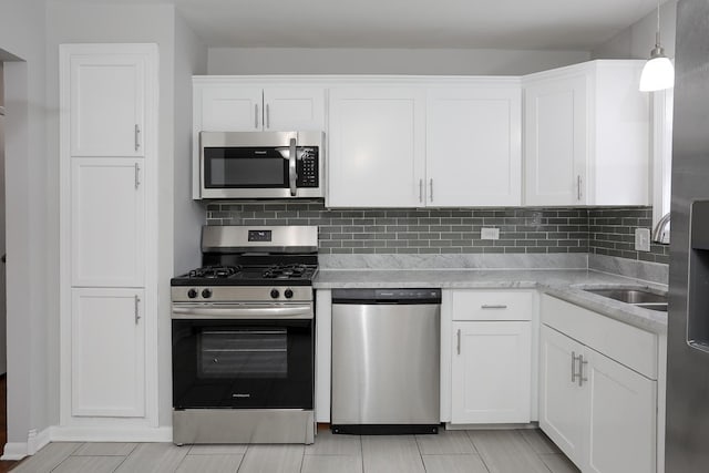 kitchen with light stone counters, white cabinets, appliances with stainless steel finishes, decorative backsplash, and decorative light fixtures