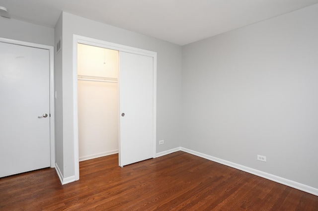 unfurnished bedroom with a closet, baseboards, and dark wood-style flooring