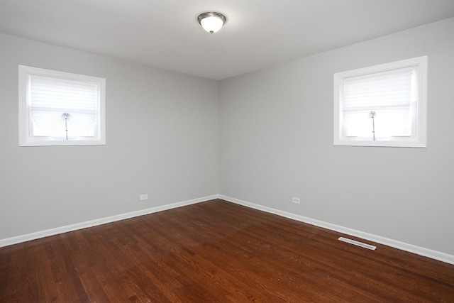 empty room with dark wood-type flooring, a healthy amount of sunlight, visible vents, and baseboards