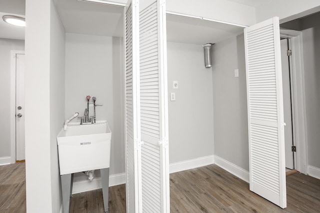 interior space with a sink, laundry area, baseboards, and wood finished floors