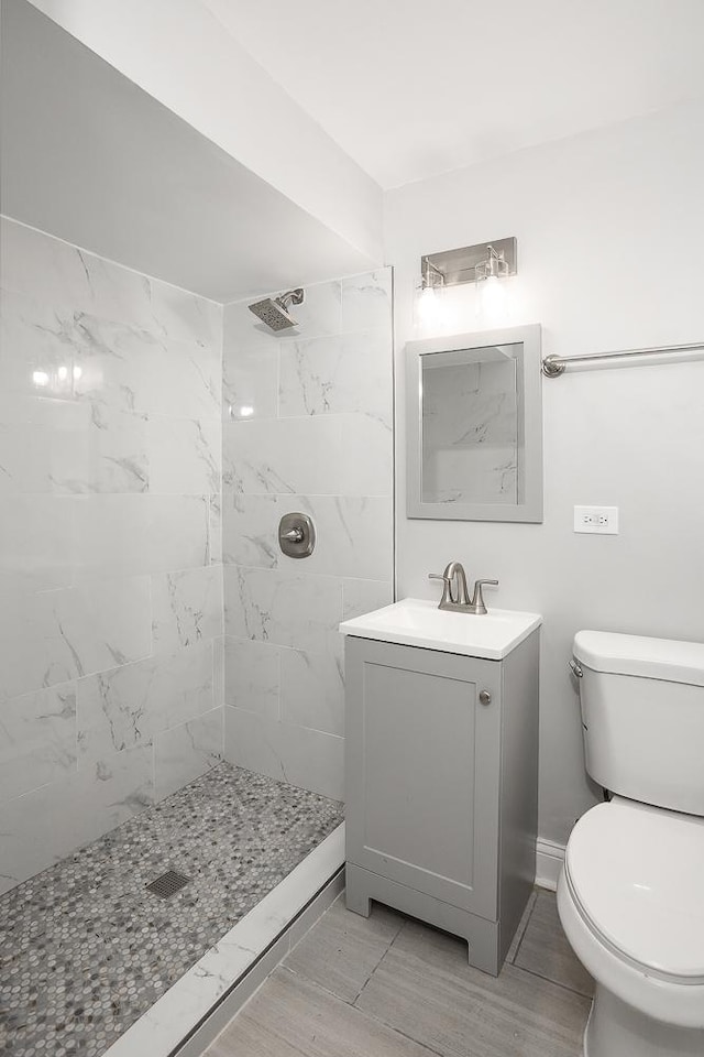 full bathroom featuring toilet, tiled shower, and vanity