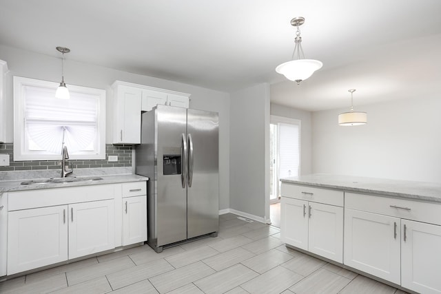 kitchen with a sink, white cabinetry, stainless steel refrigerator with ice dispenser, backsplash, and pendant lighting