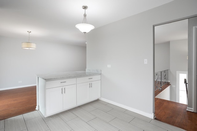 kitchen featuring wood finish floors, pendant lighting, white cabinets, light stone countertops, and a peninsula