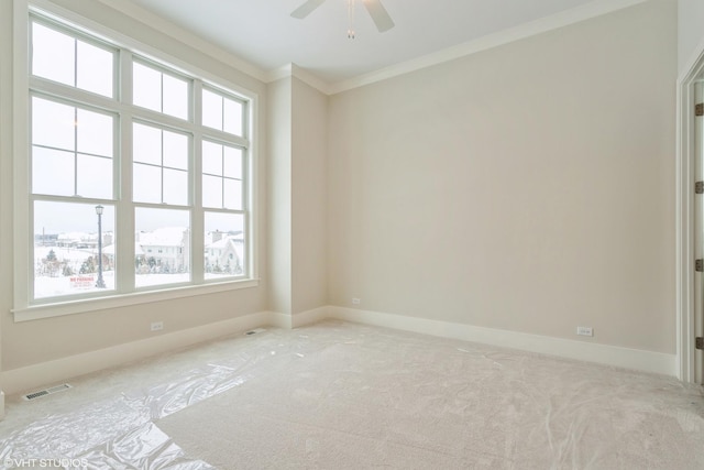 empty room with ceiling fan, light colored carpet, visible vents, baseboards, and ornamental molding