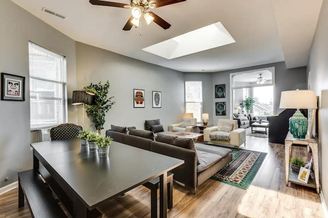 living area with light wood finished floors, a skylight, visible vents, and a ceiling fan