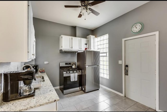 kitchen with stainless steel appliances, white cabinetry, a sink, light stone countertops, and under cabinet range hood