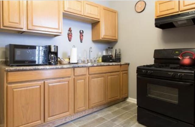 kitchen featuring light tile patterned floors, black appliances, a sink, and under cabinet range hood