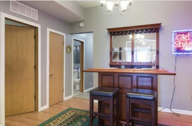 bar featuring baseboards, visible vents, wood finished floors, a bar, and a notable chandelier