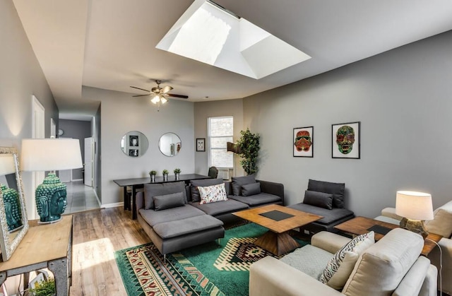 living area featuring ceiling fan, a skylight, wood finished floors, and baseboards