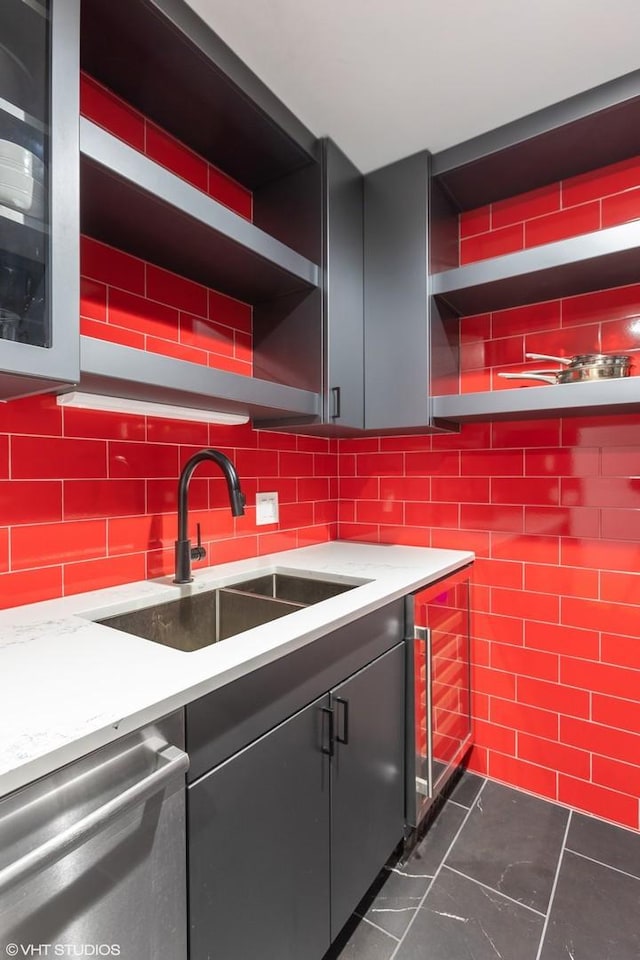 kitchen with light stone counters, a sink, stainless steel dishwasher, and open shelves