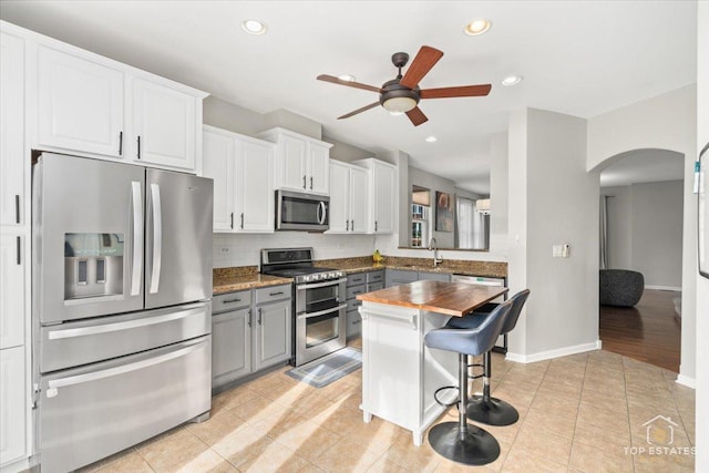 kitchen with a breakfast bar, butcher block counters, gray cabinetry, appliances with stainless steel finishes, and white cabinets