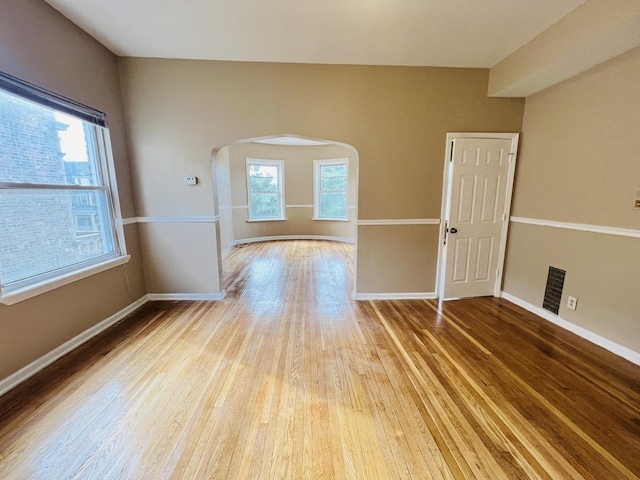 unfurnished room with light wood-style floors, arched walkways, visible vents, and baseboards