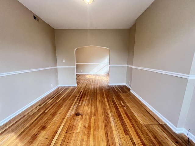 spare room featuring arched walkways, wood finished floors, and baseboards