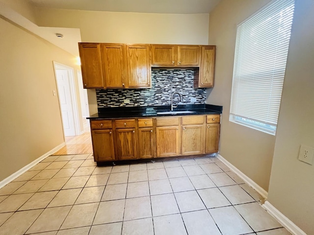 kitchen with brown cabinetry, dark countertops, a sink, and backsplash